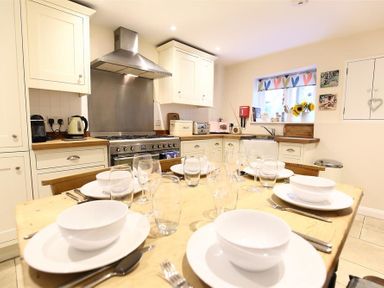 A kitchen with a dining table set with white plates and bowls and a stove with a stainless steel hood