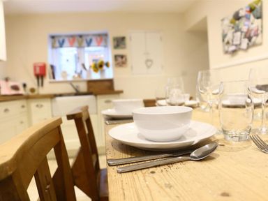 A kitchen with a wooden dining table set with white bowls plates cutlery and glasses at Hare House in Chipping Norton