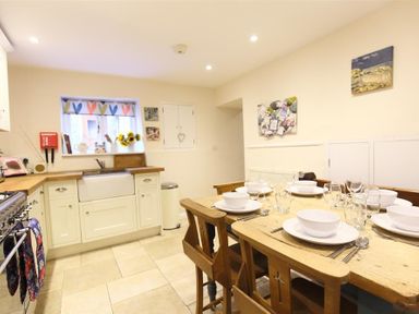 A kitchen with a wooden dining table set for six and white cabinets at Hare House in Chipping Norton