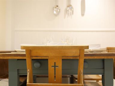 A wooden chair with a cross design at a wooden dining table with plates and glasses at Hare House in Chipping Norton