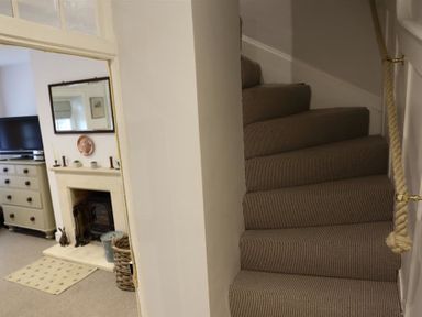 A carpeted staircase with rope handrail next to a room with a fireplace, TV, and chest of drawers at Hare House in Chipping Norton