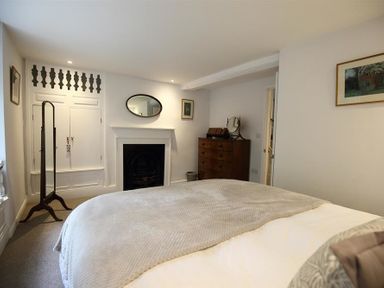 A bedroom with a bed a fireplace a wooden dresser and a standing mirror at Hare House in Chipping Norton
