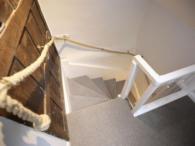 A spiral staircase with carpet and a rope handrail next to a wooden door at Hare House in Chipping Norton