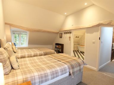 A bedroom with two single beds next to a window and an open door showing a bathroom with a bathtub at Hare House in Chipping Norton