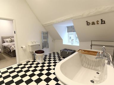 A bathroom with a bathtub toilet and a checkered floor next to a bedroom at Hare House in Chipping Norton