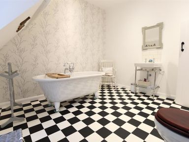 A bathroom with a freestanding bathtub a sink with a mirror a chair and a black and white checkered floor at Hare House in Chipping Norton