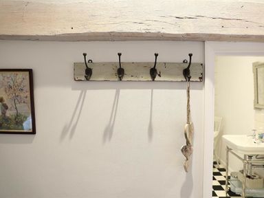 A wall with four metal hooks on a wooden board and a hanging decoration with hearts next to a doorway showing part of a bathroom at Hare House in Chipping Norton