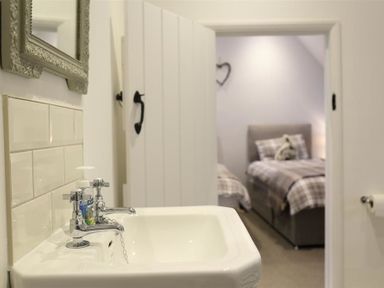 A bathroom sink with taps and soap dispenser with a partially open door leading to a bedroom with two beds at Hare House in Chipping Norton