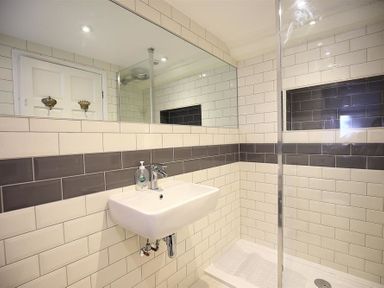A bathroom with a wall-mounted sink a glass shower enclosure and rectangular tiles at Hare House in Chipping Norton