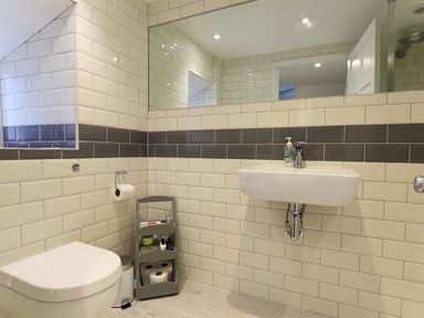 A bathroom with a wall-mounted sink toilet a small shelf with toiletries and toilet paper at Hare House in Chipping Norton