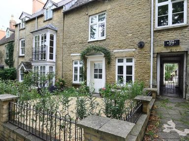 Stone exterior of a house with white-framed windows and door with a small garden and paved pathway on New Street