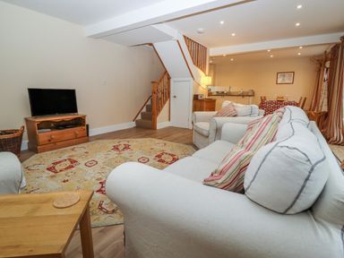 A living area with a sofa a chair a television on a wooden stand a rug and stairs at The Cottage At Barrow Mead in Bath