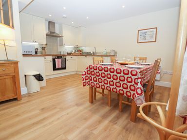 A kitchen with wood cabinets and a dining table with a red and white tablecloth at The Cottage At Barrow Mead in Bath