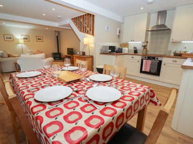 A dining table with plates glasses and cutlery in a kitchen and living room area at The Cottage At Barrow Mead in Bath