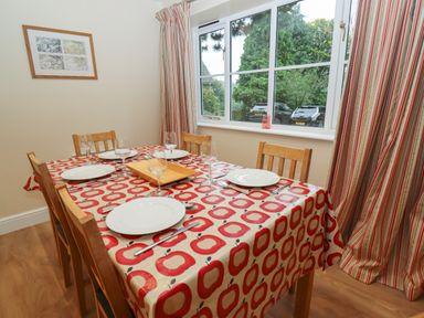 A dining room with a table set for five people near a window with striped curtains at The Cottage At Barrow Mead in Bath