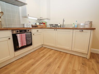 A kitchen with wooden floor white cabinets an oven a sink and various items on the countertop at The Cottage At Barrow Mead in Bath