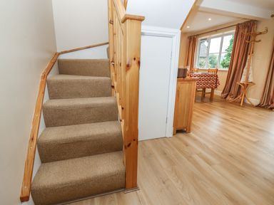 A staircase with carpet next to a dining area with a table and chairs and windows with curtains at The Cottage At Barrow Mead in Bath