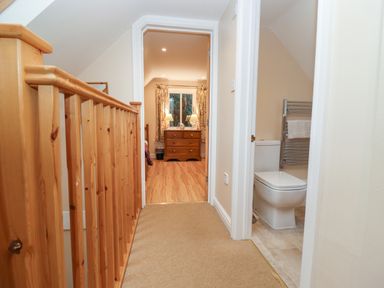 A hallway with wooden banister leading to a bedroom and a bathroom with a toilet at The Cottage At Barrow Mead in Bath