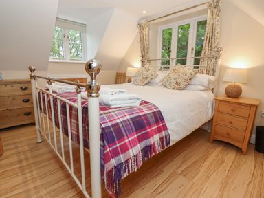 A bedroom with a metal bed frame floral pillows wooden nightstands and a plaid blanket at The Cottage At Barrow Mead in Bath