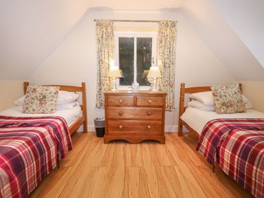 A bedroom with two single wooden beds a wooden chest of drawers with two table lamps and floral curtains at The Cottage At Barrow Mead in Bath