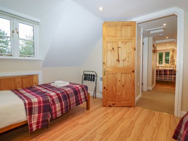 A bedroom with a single bed covered by a red plaid blanket and a wooden door opening to a hallway leading to another bedroom at The Cottage At Barrow Mead in Bath