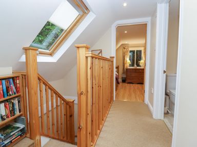 A hallway with a wooden staircase and bookshelf leading to a bedroom and bathroom at The Cottage At Barrow Mead in Bath