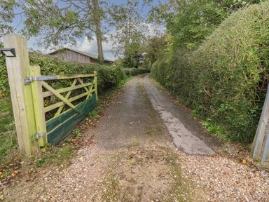 A gravel driveway with a wooden gate and hedges along the sides at The Cottage At Barrow Mead in Bath