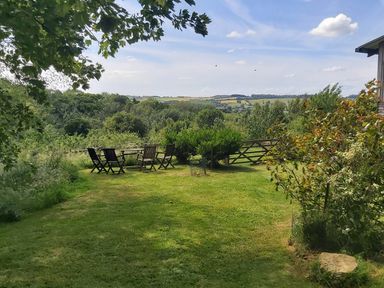 A grassy garden with wooden chairs and a table near bushes and a gate at The Cottage At Barrow Mead in Bath