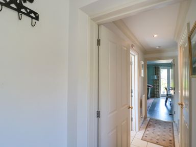 A hallway with white doors a rug on the tiled floor and a view into a room with dark wooden flooring at Batemans in Nailsworth