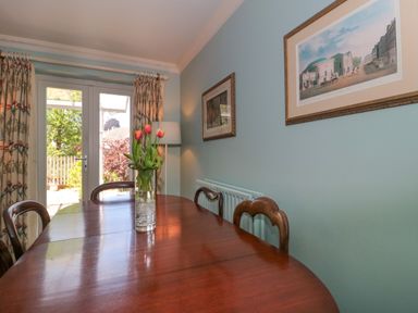 A dining room with a wooden table and chairs with flowers in a vase on the table and framed pictures on the wall at Batemans Nailsworth