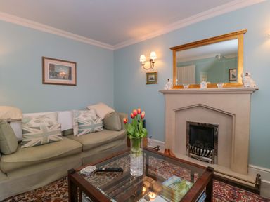 A living room with a green sofa, cushions, a glass coffee table with flowers, and a fireplace with a mirror above at Batemans Nailsworth