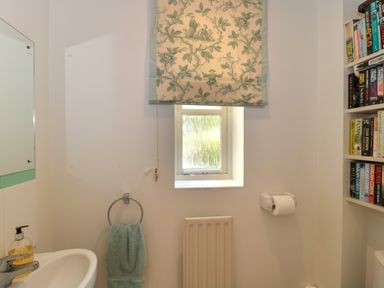 A bathroom with a small window and printed curtain a towel ring with a towel and a wall-mounted bookshelf at Batemans Nailsworth