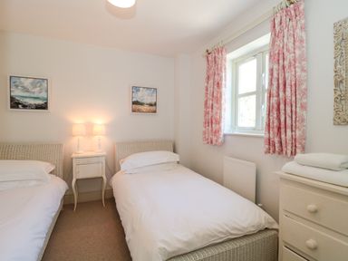 A bedroom with two single beds a nightstand with two lamps a window with curtains and a dresser with folded towels at Batemans in Nailsworth