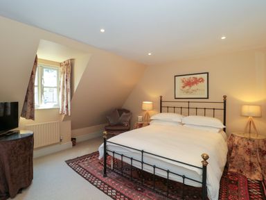 A bedroom with a bed framed by two lamps on side tables and a chair near a window at Batemans in Nailsworth
