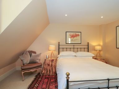A bedroom with a bed an armchair two bedside tables with lamps and framed pictures on walls at Batemans Nailsworth