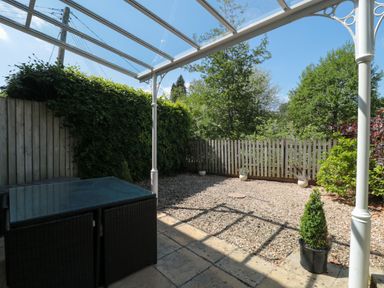 A backyard with a glass canopy a patio table gravel ground and a wooden fence at Batemans Nailsworth