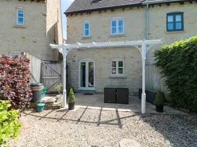 A stone house with a small patio covered by a white pergola and surrounded by bushes at Batemans Nailsworth