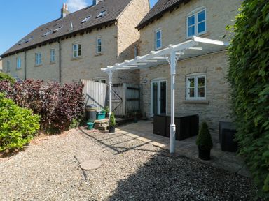 A stone house with a small patio and gravel yard with plants and a white pergola at Batemans in Nailsworth