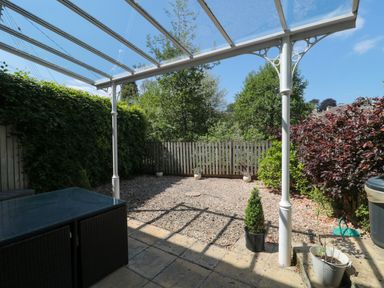 An outdoor patio area with a glass roof and plants along a wooden fence at Batemans Nailsworth