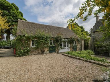 A stone building with a tiled roof and climbing plants near a gravel area at Hazel Manor Wing in Painswick