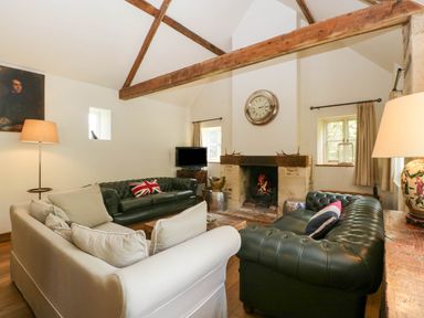 A living room with leather sofas a fireplace and wooden beams at Hazel Manor Wing in Painswick