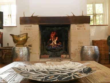 A stone fireplace with a fire burning and decorative items on either side of it at Hazel Manor Wing in Painswick