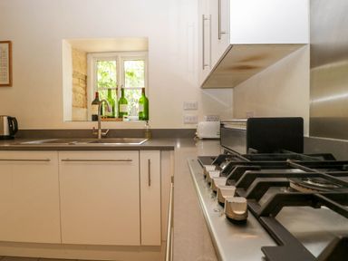 A kitchen with a sink under a window and a gas stove on the counter at Hazel Manor Wing in Painswick