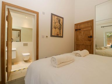 A bedroom with a bed with rolled towels on top a wooden door a framed artwork and an open door showing a bathroom at Hazel Manor Wing in Painswick