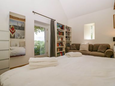 A bedroom with a bed with folded towels a sofa a bookshelf and a door with a window at Hazel Manor Wing in Painswick