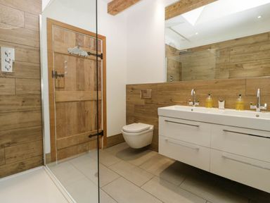 A bathroom with a wall-mounted toilet a double sink vanity and a shower at Hazel Manor Wing in Painswick
