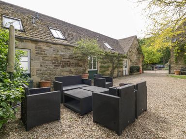 An outdoor seating area with black wicker furniture on gravel outside a stone building at Hazel Manor Wing in Painswick