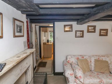 A living room with floral sofa cushions a fireplace and framed pictures on the wall at Newbury Cottage in Bourton-On-The-Water