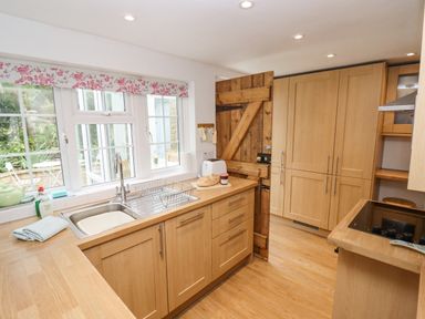 A kitchen with wooden cabinets a sink toaster and a wooden door at Newbury Cottage in Bourton-On-The-Water