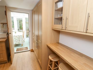 A kitchen with wooden cabinets a countertop stools and a doorway leading to a dining area at Newbury Cottage in Bourton-On-The-Water